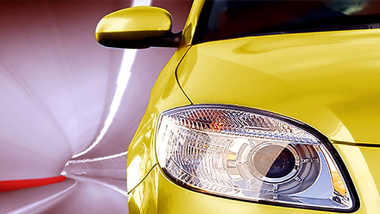 Front of a yellow car driving through a tunnel, right front light and wing mirror in view