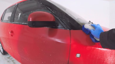 Hand washing red car exterior with blue sponge