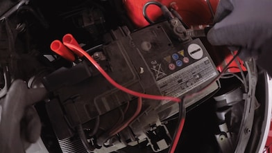 Hands connecting red and black charger cables to car battery terminals