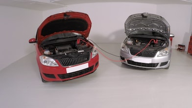 Red and grey cars with open hoods connected by jumper cables for battery jump start