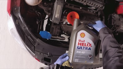 Hands in gloves pouring Shell Helix Ultra 5W-40 synthetic motor oil into car engine