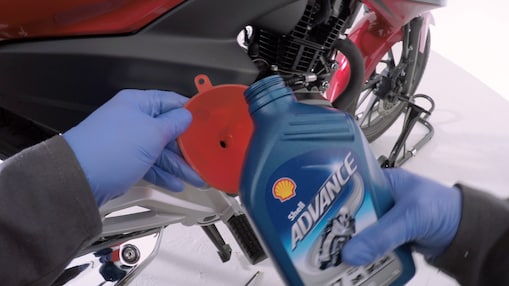 Hands in blue gloves ready to pour Shell Advance motor oil into red motorcycle engine