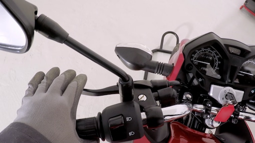 Gloved hand gripping clutch lever on red motorcycle handlebar