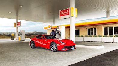 A red Ferrari sitting on a Shell station forecourt with a man leaning on a petrol pump
