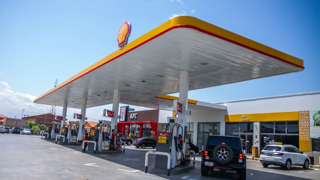 Shell service station forecourt at dusk with fuel pumps, attendants, and customer vehicles