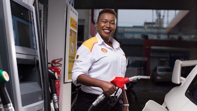 Shell petrol station attendant refueling white car with fuel nozzle